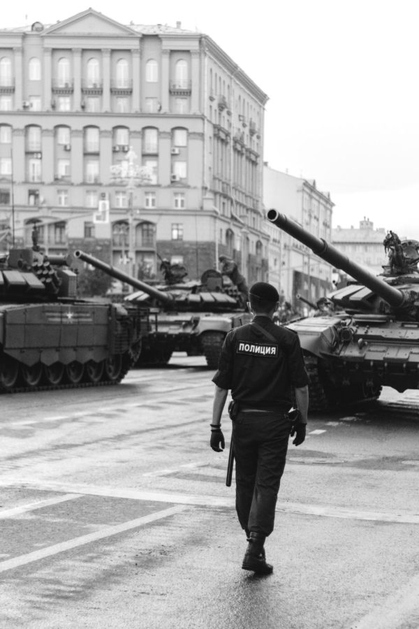 A Russian police officer stands ready in front of multiple tanks.
